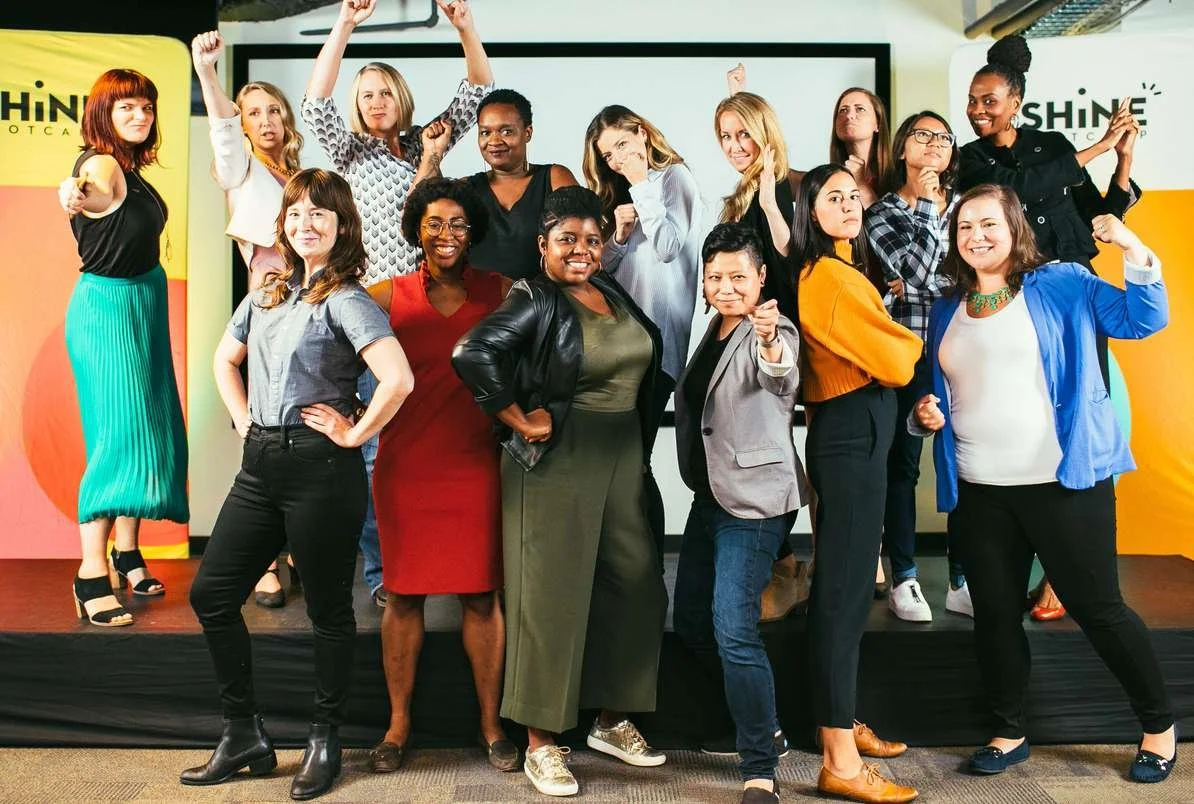 Shine Bootcamp participants celebrating with arms raised in front of the Shine backdrop