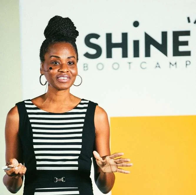 A Shine speaker in a striped top gesturing in front of the Shine Bootcamp logo