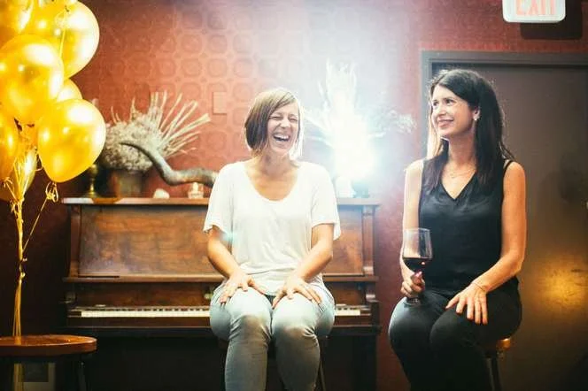 Two Shine participants chatting beside a piano under gold balloons